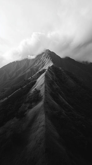 Black-and-white aerial view of a sharp mountain ridge cutting through low clouds in moody light.