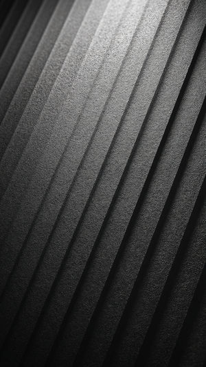 Close-up of abstract black textured diagonal ridges forming a dark minimalist gradient background wallpaper.