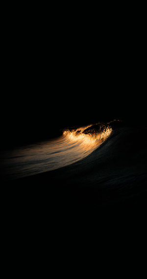 Dark minimalist ocean wave lit by molten-gold highlights, curling across a deep black sea at night.