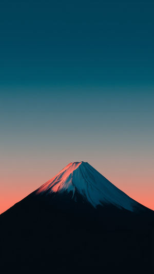 Mount Fuji snow-capped peak illuminated by pink sunrise light against a teal gradient sky and dark mountain silhouette.