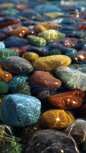 Close-up view of multicolored smooth river pebbles submerged in flowing water reflecting sunlight