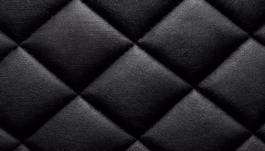 Close up of black quilted fabric in a repeating diamond pattern, with fine woven texture and deep seams.