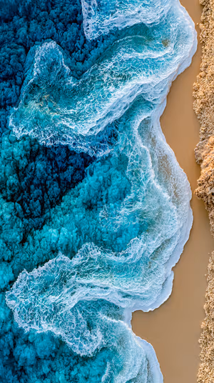 Aerial view of turquoise ocean waves and foamy surf along a sandy coastline in ultra HD 8K image