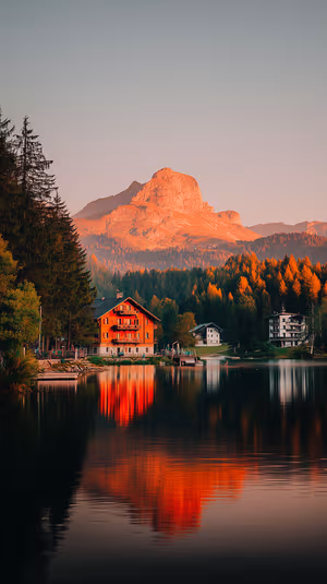 Cinematic alpine chalet and mountain lake centered on warm orange background with mirror reflection, ultra HD image.