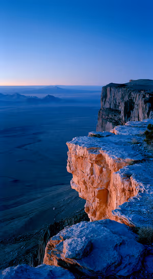 Cinematic canyon cliffs above a blue hour plateau with warm orange rock and distant mountains in an ultra HD landscape.