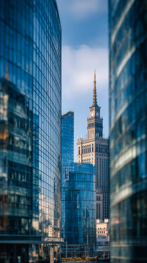 Architectural clock tower framed by reflective blue glass towers on a crisp urban skyline ultra hd 8K image.