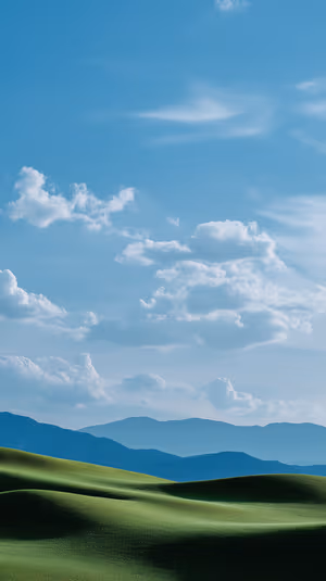 Minimalist landscape: sunlit rolling green hills and distant blue mountains beneath a bright blue sky with soft white clouds.