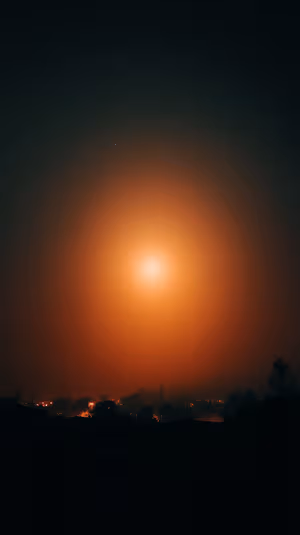 Cinematic glowing orb centered on a deep orange night sky with foggy halo and silhouetted town, ultra HD phone background.