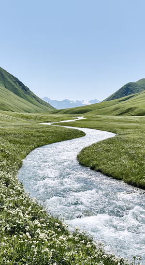 Minimalist valley stream flowing through green mountain meadows beneath a pale blue sky.
