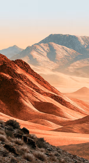 Retro mountain landscape in terracotta and red tones with layered ridges and a muted peach sky