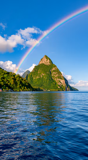 Nature mountain landscape with a rainbow over blue ocean water in a vibrant scenic aesthetic.