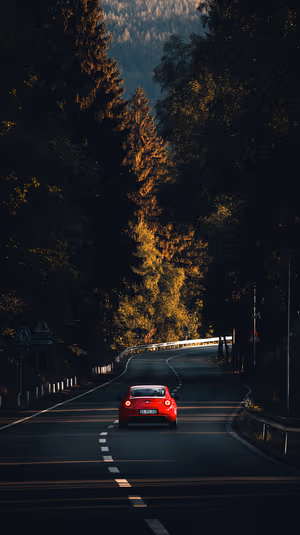 Cinematic red coupe on winding mountain road through golden hour forest ultra HD background