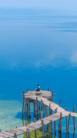 Minimalist lake pier with a lone figure centered on a turquoise blue background; ultra HD 8K mobile lock screen image.
