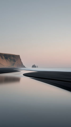 A serene black sand beach at dawn in Iceland, with reflective waters, basalt cliffs and distant sea stacks.