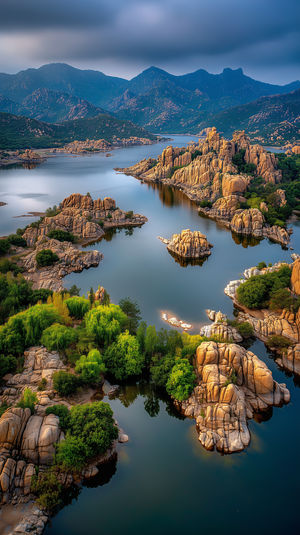Aerial shot of a mountain lake with granite rock islands, lush green trees, and calm reflective water.