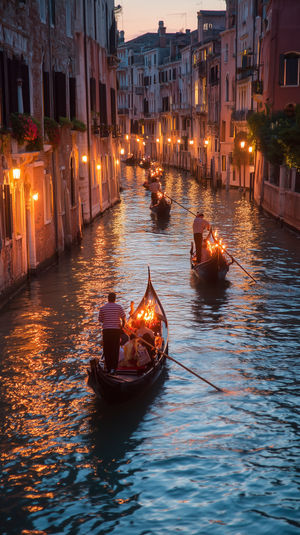 A line of gondolas passing under glowing street lamps along a narrow Venetian canal at sunset, water reflecting warm lights.