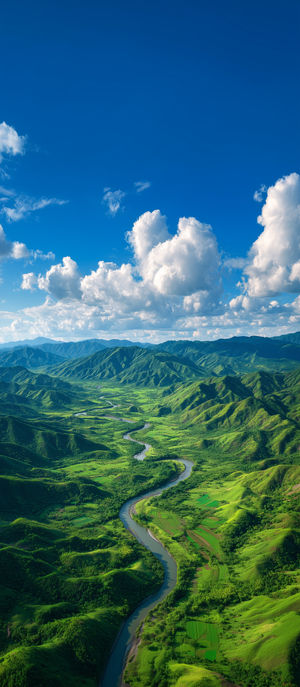 Aerial perspective of a winding river flowing through lush green mountains beneath a vivid blue sky dotted with white clouds.