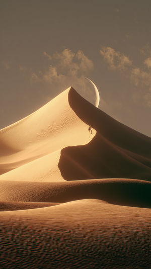 A lone climber ascends a golden sand dune at sunset as a crescent moon rises behind it over a vast desert.