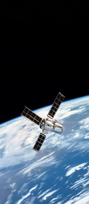 A high-resolution image of a satellite with four solar panel wings orbiting Earth against the black expanse of space.