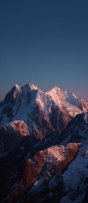 Snow-covered mountain peaks bathed in pink alpenglow under a clear dusky sky at sunset