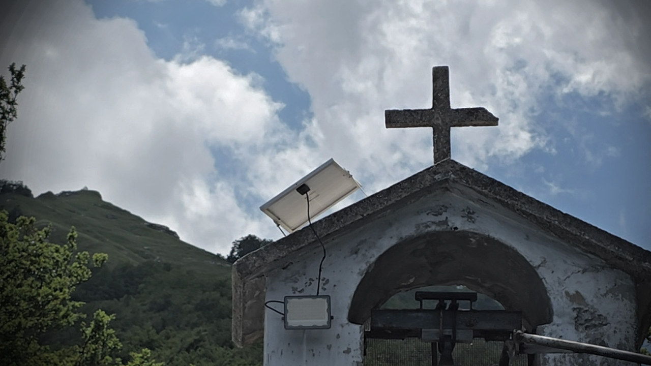 Il campanile a vela dell’Eremo di Santa Colomba con la campana e la croce, la montagna sullo sfondo