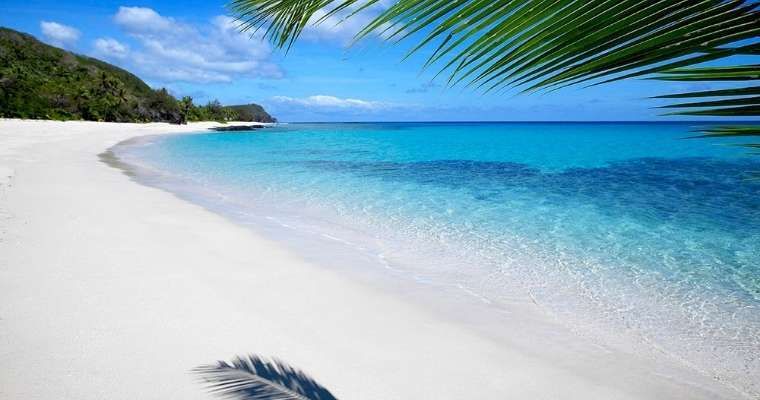 Crystal clear waters of Fiji with white sand beaches and palm trees overhead, find Fiji Travel Expert here