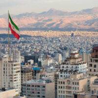 Waving Iran flag above skyline of Tehran at sunset.