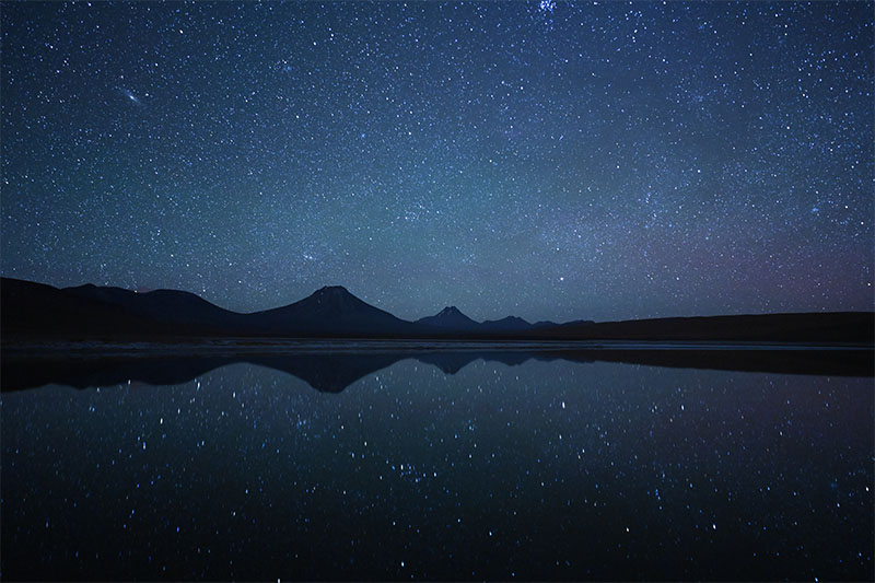 Image Credit: Taylor Gray Mountains beneath starry sky reflected in water, shot in the Atacama Desert with the Nikon Z 20mm f/1.8 S lens
