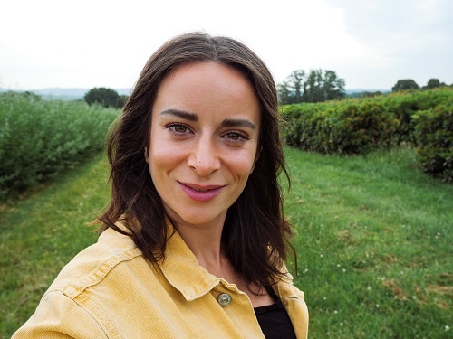 Selfie of young woman with dark hair standing in a Greenfield, shot with the Panasonic G100 Mirrorless Camera