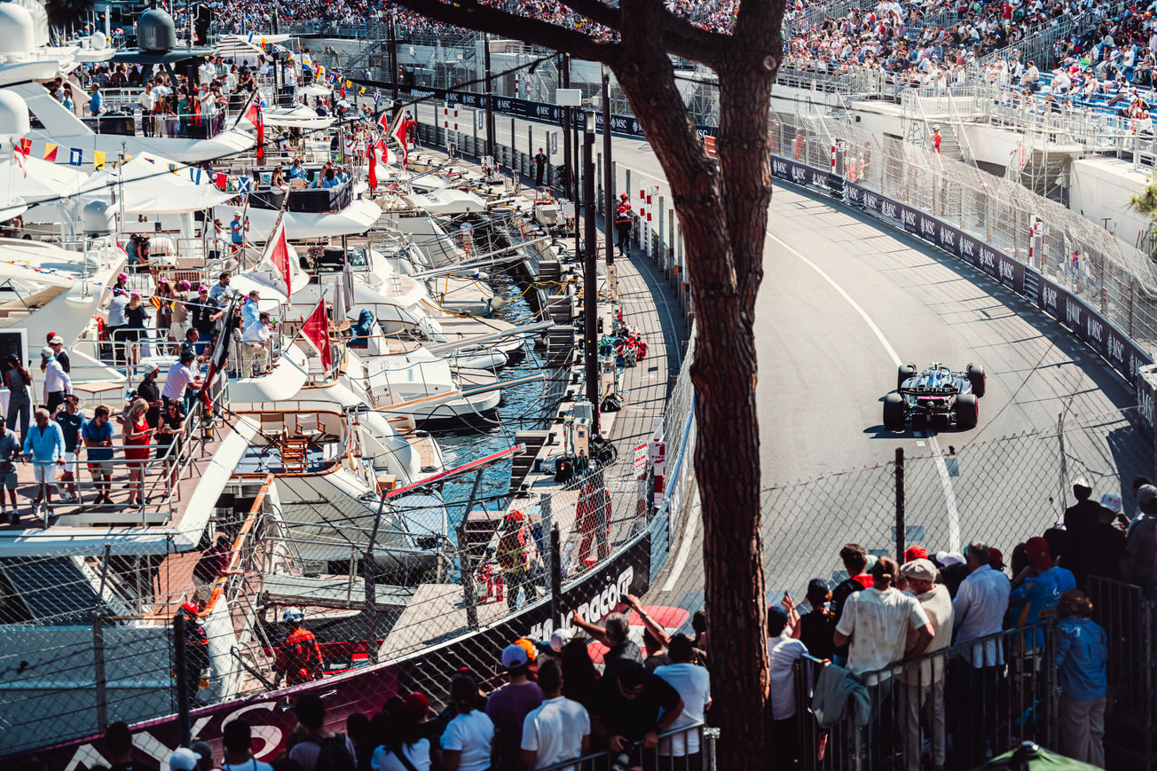 Spectators on a yacht see an Alpine F1 car racing through the harbor of Monaco