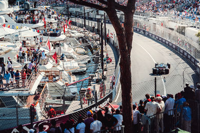 Spectators on a yacht see an Alpine F1 car racing through the harbor of Monaco