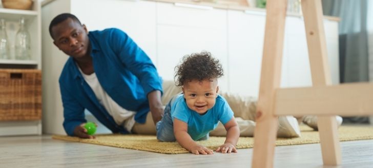 Baby crawling on floor with Dad watching