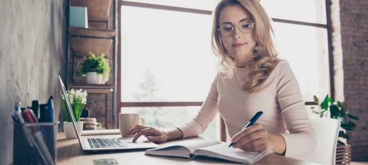 Woman using a laptop and writing in a notebook