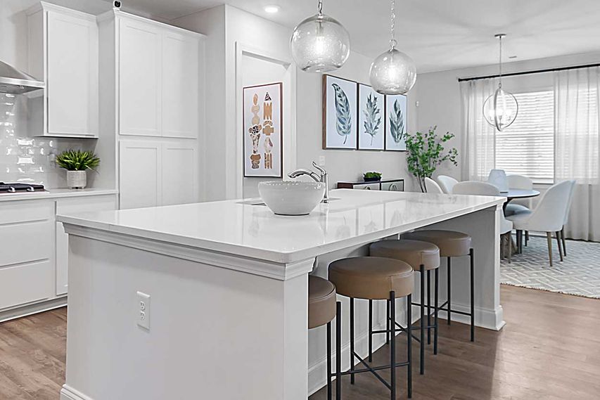 White kitchen with an island and bar seating next to a dining area.