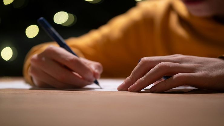 A photograph of someone writing. Their hands are the focal point of the image.