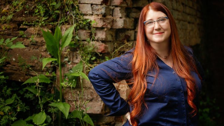 Jenn Lyons smiling in front of a brick wall with climbing plants growing on it