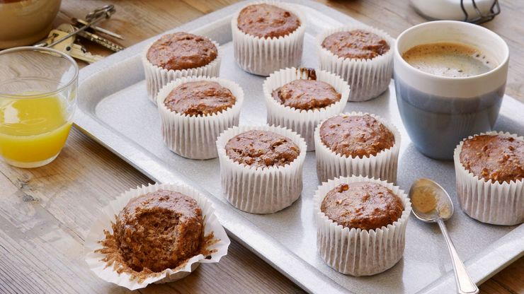 A photograph of banana muffins on a tray alongside a mug of a coffee and a glass of orange juice