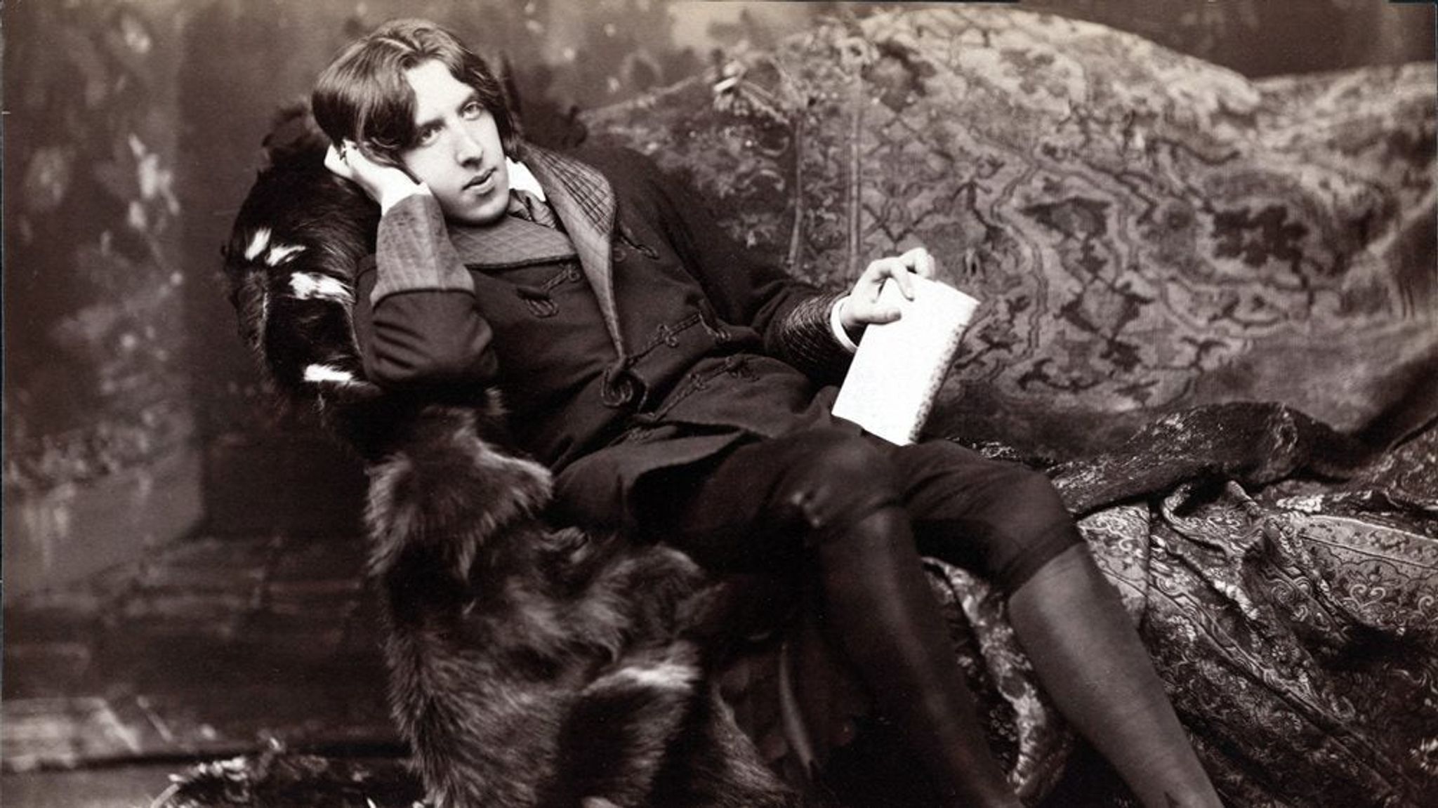 Oscar Wilde photographed sitting in a fur covered chair.