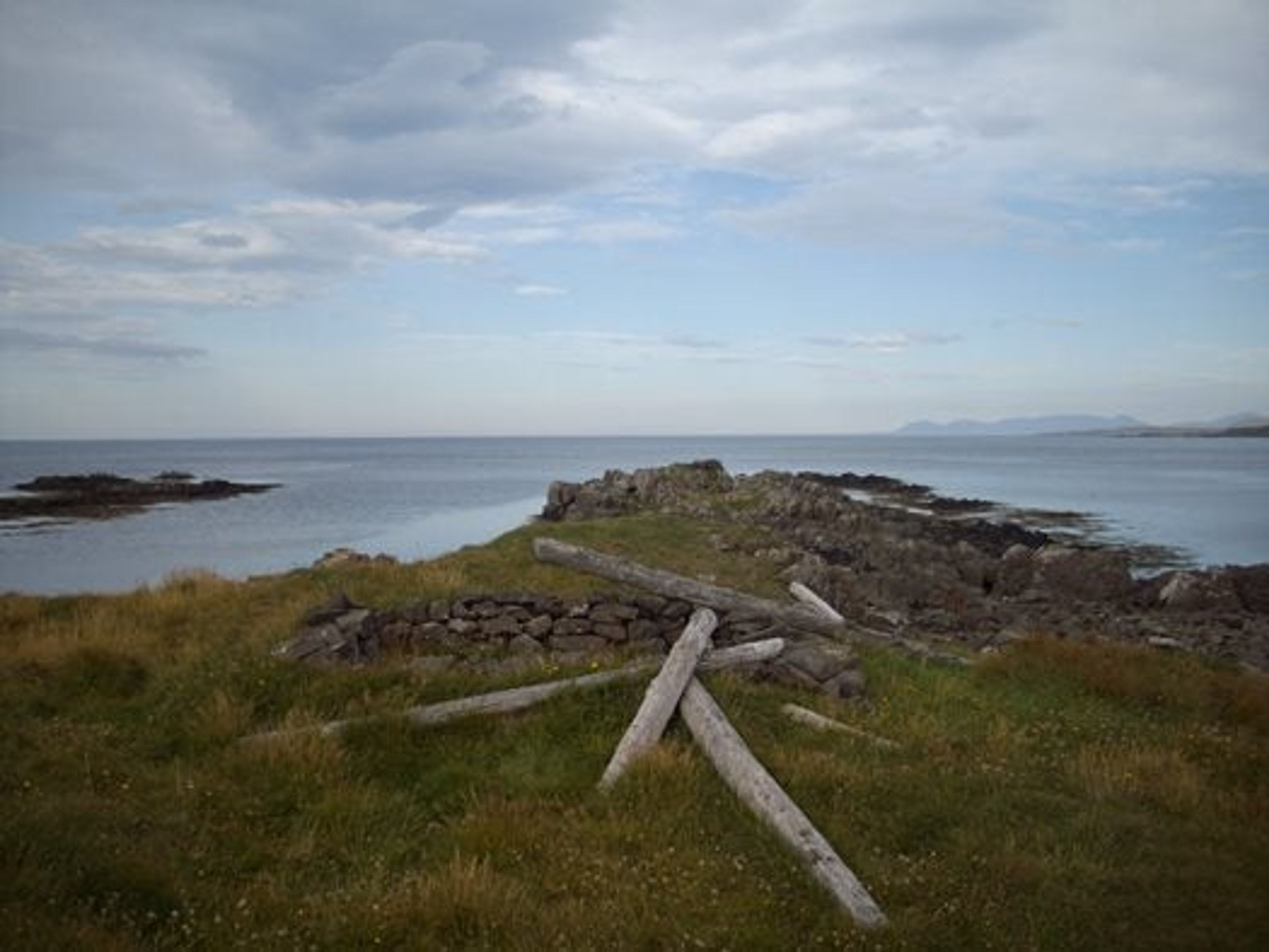 A hill with a dissembled old workshop, old stones assembled as bricks and old wooden logs. 