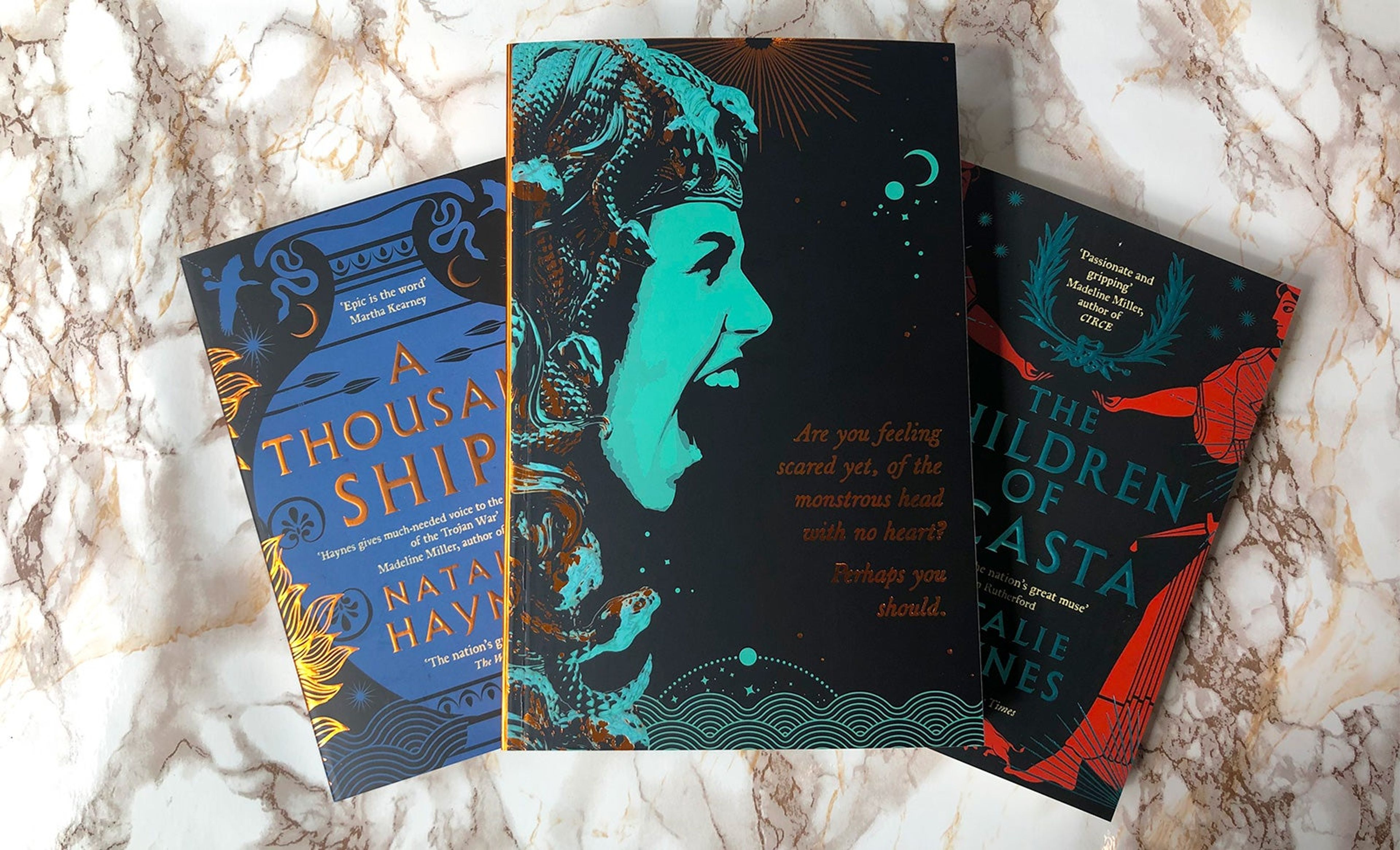 A proof copy of Stone Blind and paperback copies of A Thousand Ships and The Children of Jocasta on a marble counter.