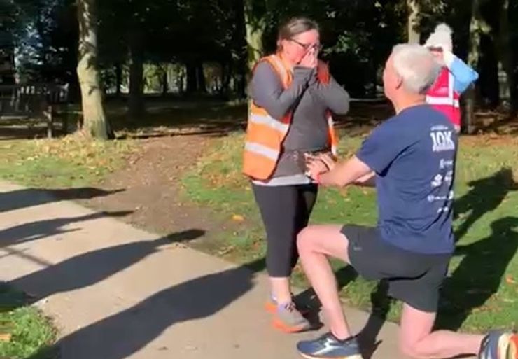 Photograph of a man on bended knee proposing to a woman in a high vis jacket