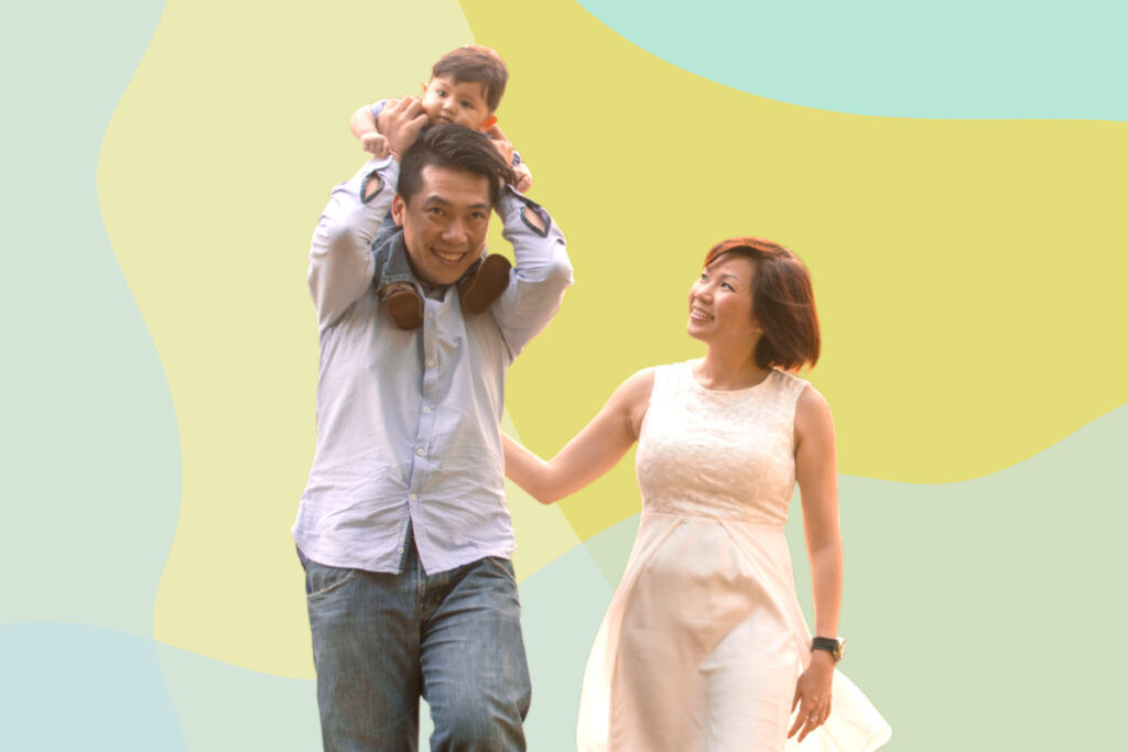 Picture of a cute baby riding on his father's shoulders while his mom is looking. 