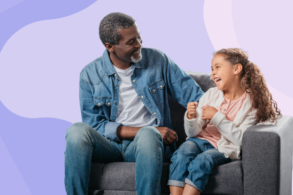 A young girl and older man laughing together on a couch