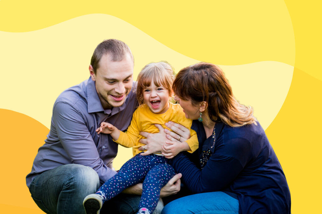 Man and woman holding a child wearing a yellow long sleeved shirt.