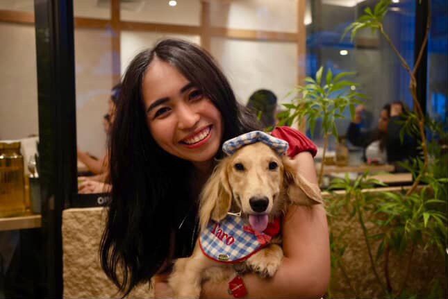 A woman holding Taro, a dachshund in a checkered hat, at a pet-friendly cafe