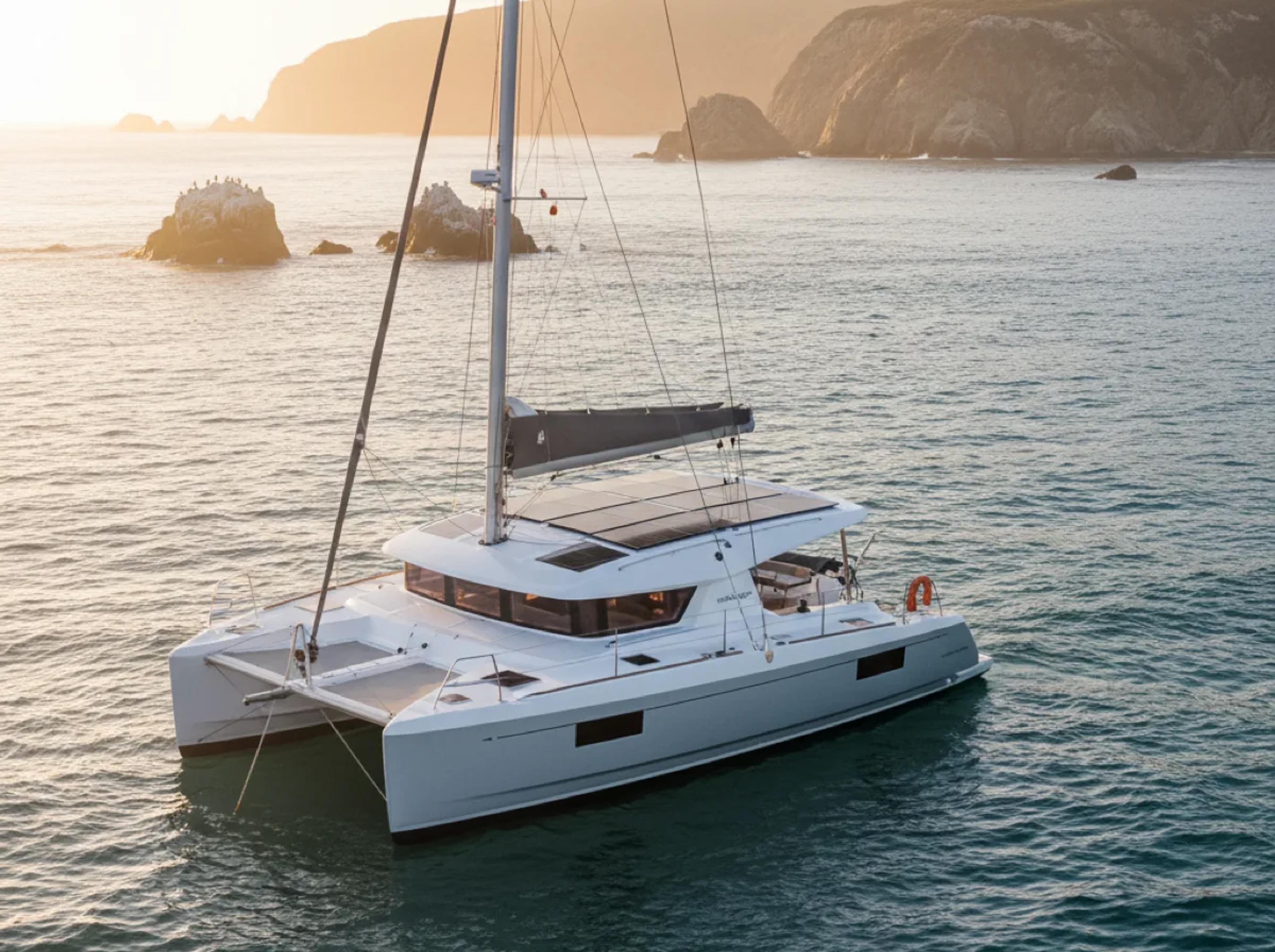 Catamaran at anchor in a Southern California cove with solar panels mounted on the roof, late-afternoon light