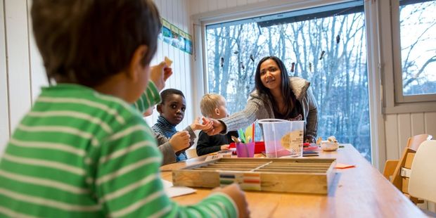 Barnehagelærer snakker med barn rundt bord i barnehage. Foto.