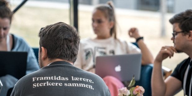 Bilde av fire studenter som jobber i gruppe. Studenten med ryggen til har en genser med teksten: Framtidas lærere. Sterkere sammen. 