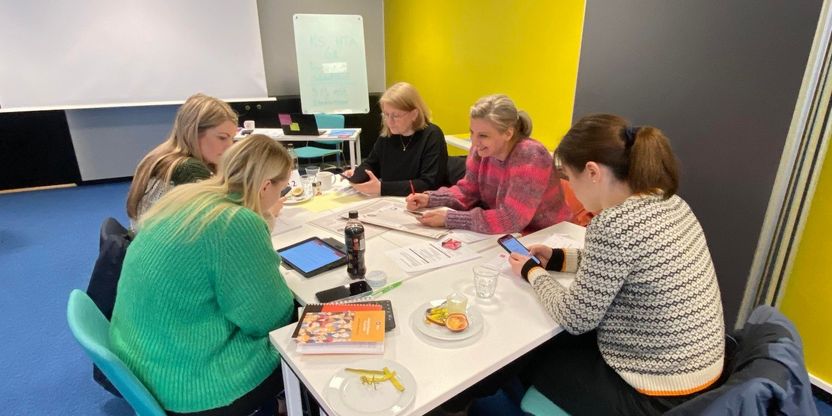 5 kvinnelige tillitsvalgte som sitter rundt et gruppebord og diskuterer/jobber med oppgaver
