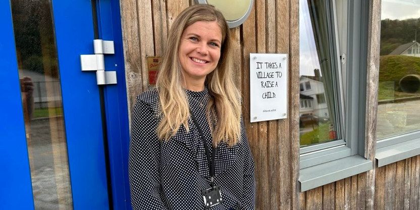 En dame med langt, lyst hår står smilende foran inngangen til en barnehage.
